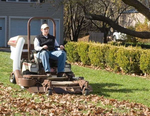 Person on a ride-on mower with a leaf collector, driving over fallen leaves