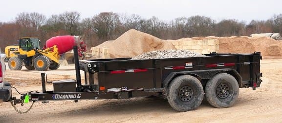 Black dump trailer parked on a materials yard with a loader in the background